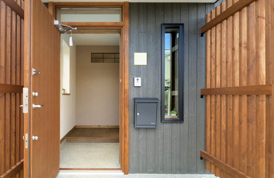 木製の目隠しルーバーと玄関ドア、こげ茶色のサイディングが調和する玄関まわり