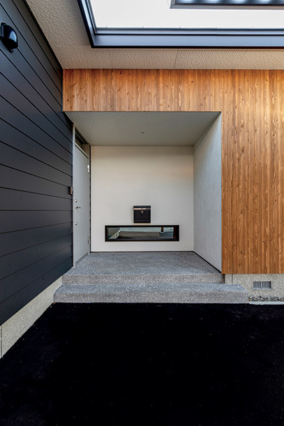 硬質なガルバリウム鋼板と温かみのある木が美しいコントラストを描く玄関ポーチ。夜は地窓から室内の灯りがこぼれる