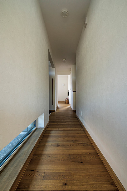 玄関から2つの個室へ延びる廊下には、地窓を採用。細長い開口からこぼれる外光が足元をやさしく照らす