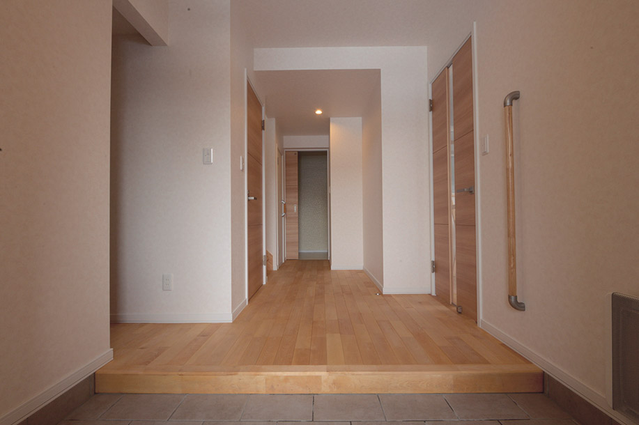 カバ無垢床と白壁でシンプルに整えた明るい玄関。左手にはベビーカーまで楽々収納できるファミリークロークがある